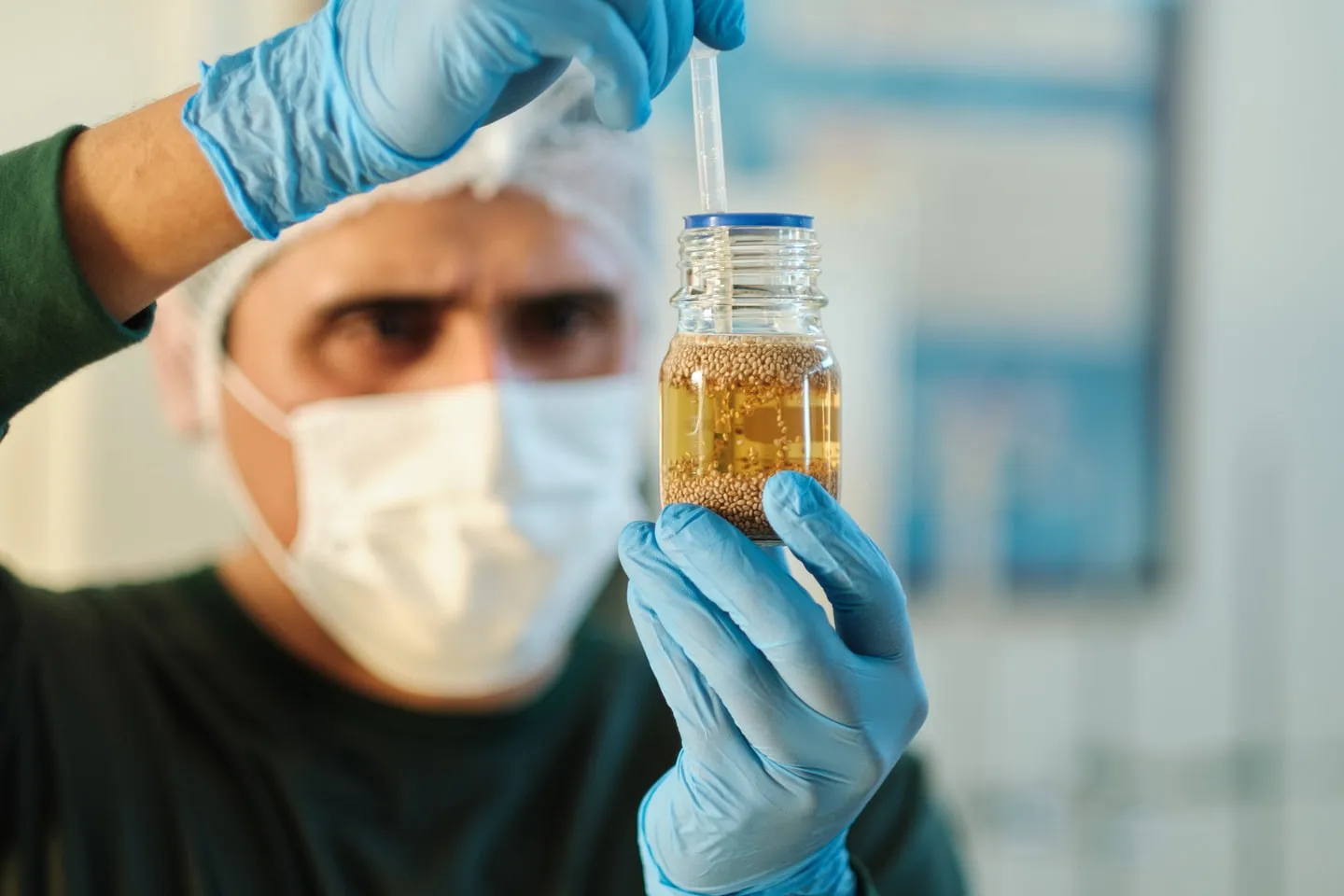 A technician inspecting a jar of chia oil with a pipette
