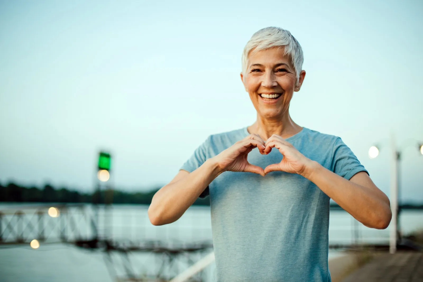 A woman forming a heart with her hands, outdoors at dusk
