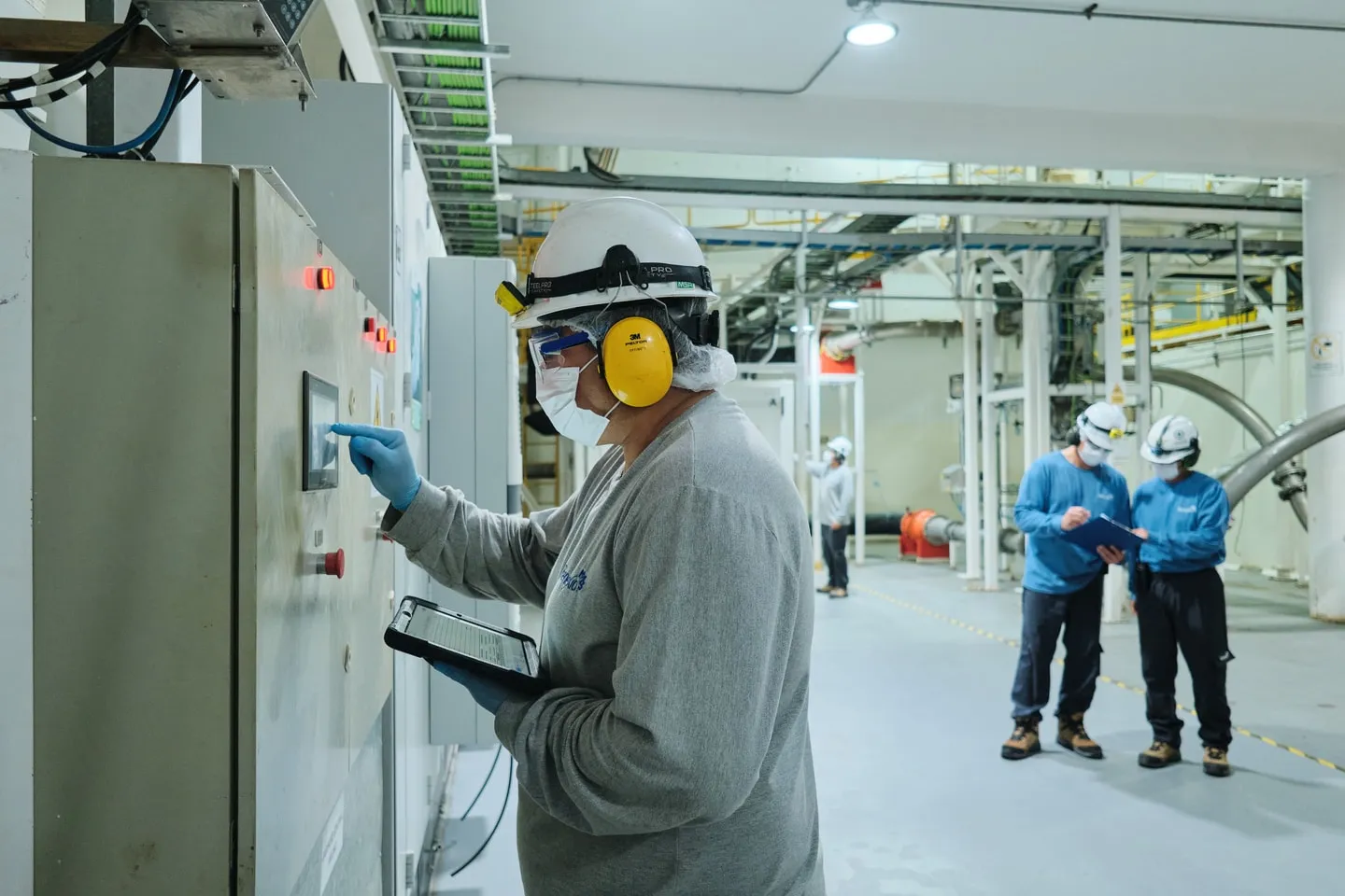 An operator with ear protection at a control panel inside the processing plant