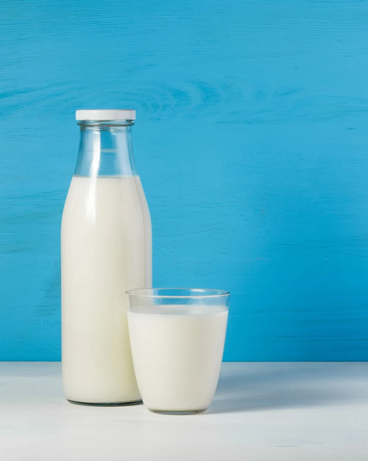 Bottle and glass of milk against a blue background