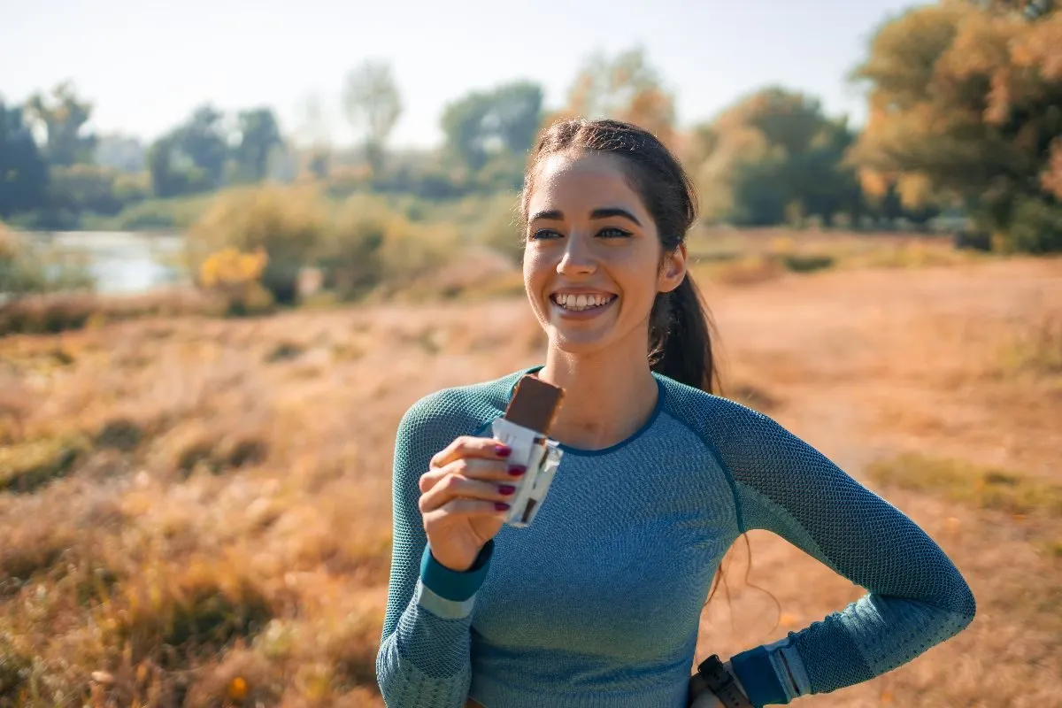 A runner smiling outdoors, holding a chocolate-coated bar