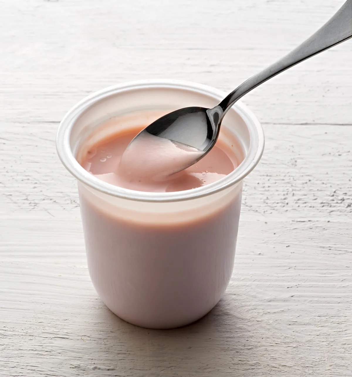 A tub of fruit yoghurt with a spoon resting in it